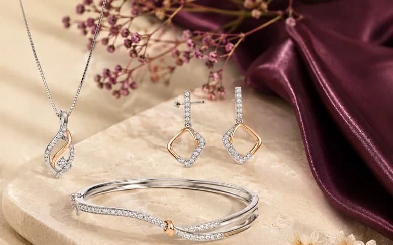 A stone-set pendant, geometric drop earrings and a slim two-tone bangle arranged on a stone slab.